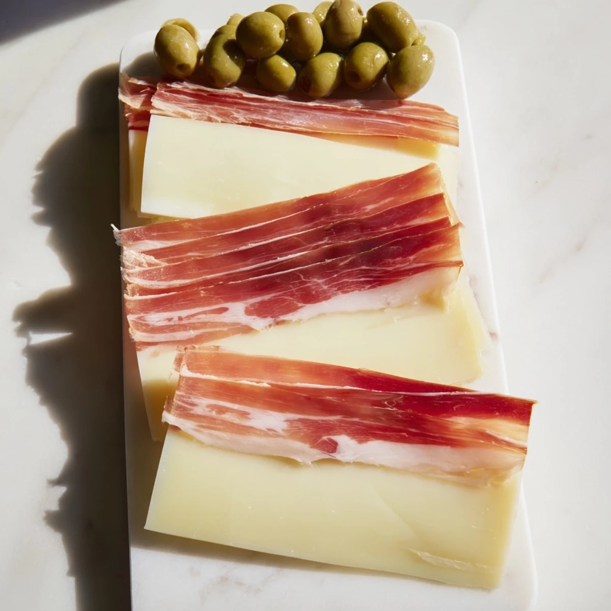 Elegant cheese board featuring the Minimalism Master: aged Comté, Jamón Ibérico, and olives, ready to serve.
