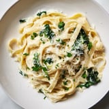 This beautiful photo shows a bowl of creamy Spinach Fettuccine Alfredo, ready to serve with extra Parmesan cheese.