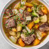 Golden-brown Welsh Cawl stew, fragrant and hearty, garnished with fresh parsley for a comforting meal.