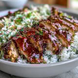 Sliced BBQ chicken, fluffy rice, and colorful roasted vegetables are layered in a bowl topped with creamy coleslaw.
