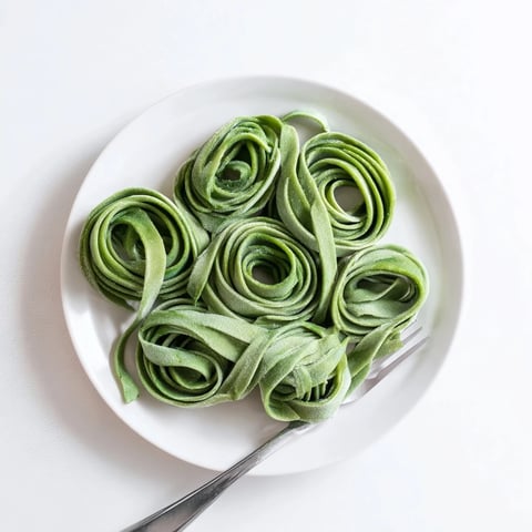 A close-up of freshly rolled spinach pasta dough sheets, vibrant green and ready for cutting into fettuccine or ravioli shapes.