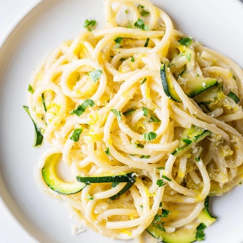 Al dente spaghetti tangled with bright spiralized zucchini in a glossy lemon butter sauce, garnished with fresh parsley.