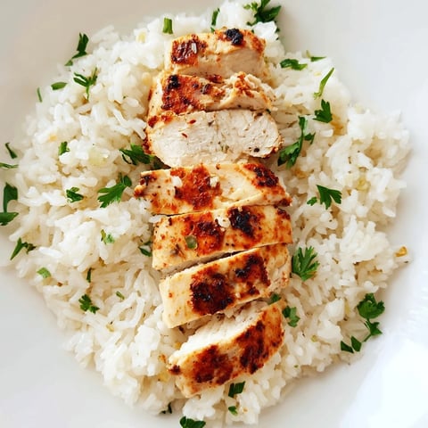 Golden-grilled chicken slices rest atop fluffy, garlic butter rice, garnished with fresh parsley and lemon wedges.