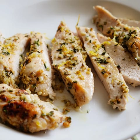 Bright yellow lemon slices garnish the moist, flavorful Greek Lemon Herb Chicken in a baking dish.