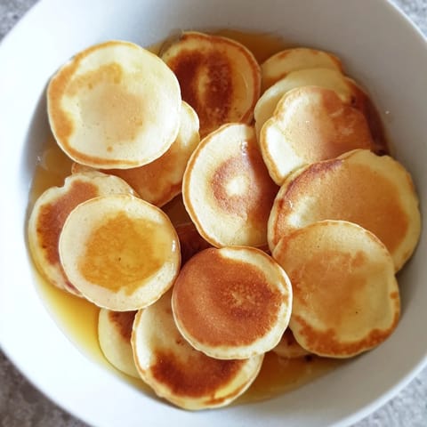 Miniature fluffy pancake cereal, swimming in milk and topped with rich maple syrup, ready to eat.