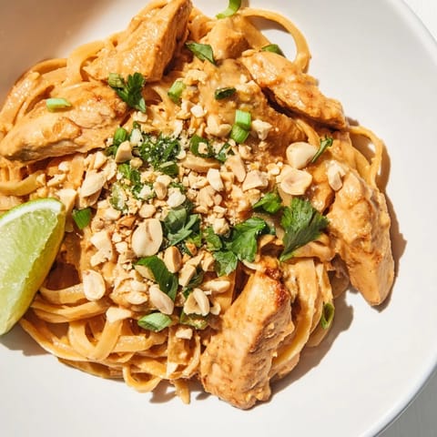 Creamy Thai peanut chicken pasta with vibrant green onions and a squeeze of lime, delicious.