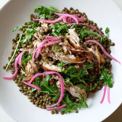 A close-up of Lentil & Chicken Spring Salad with tender lentils, juicy shredded chicken, peppery arugula, and tangy pickled onions on a white plate.  