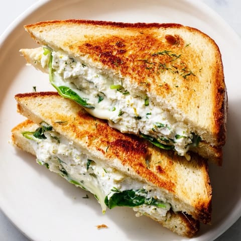 A close-up of the grilled cheese shows melted feta mixture oozing between slices, highlighting the fresh herbs and bright lemon notes.