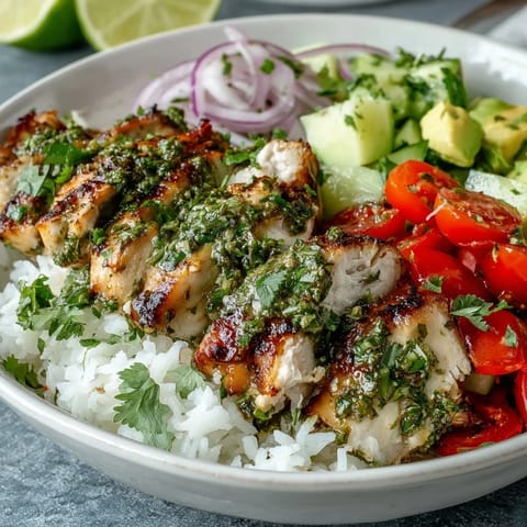 Juicy chimichurri chicken slices rest atop fluffy rice with vibrant cherry tomatoes and avocado, drizzled with fresh herb sauce.