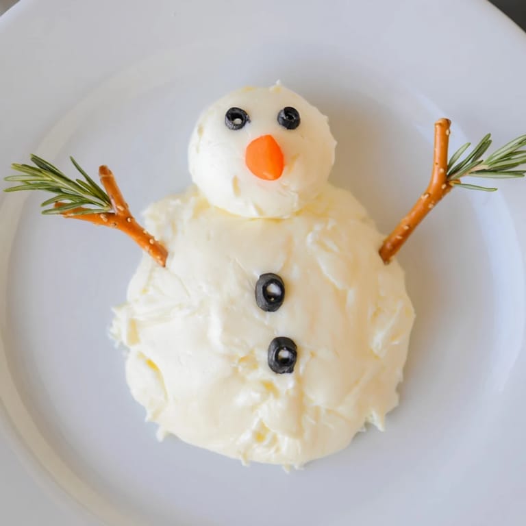 These fun Melted Snowman Cheese Bites feature creamy cheese with black olive, carrot nose, and pretzel arm details.