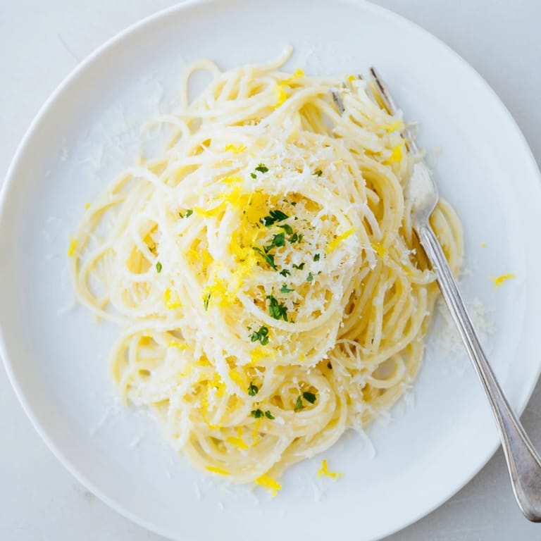 Golden-brown butter and lemon zest swirl around tender angel hair pasta, garnished with herbs and grated Parmesan cheese.