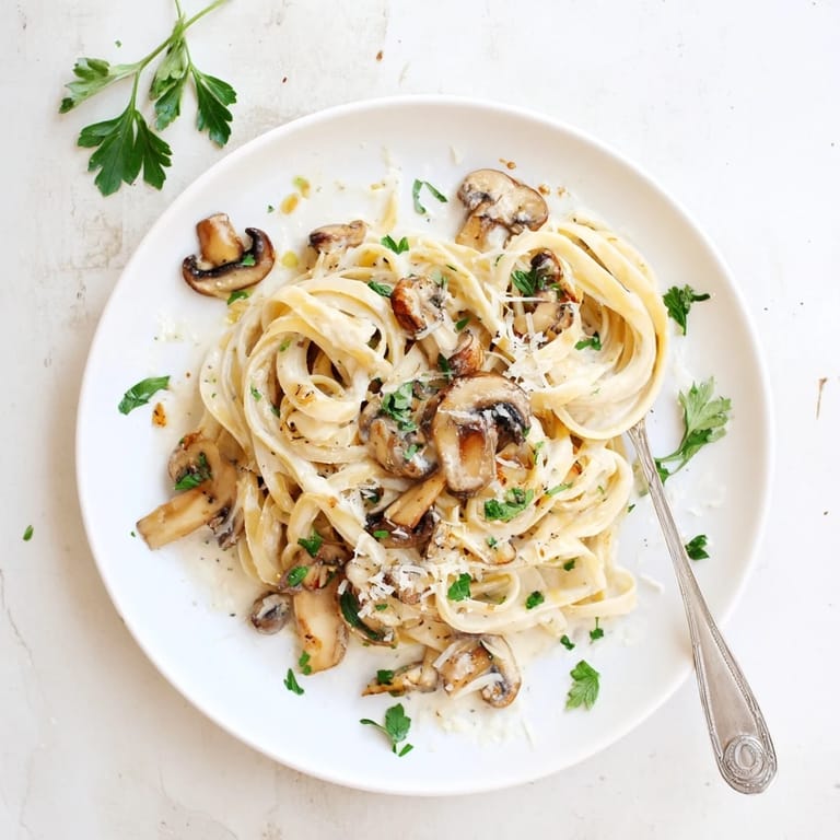A close-up of Creamy Mushroom Linguine reveals tender mushroom slices and melted Parmesan, garnished with fresh chopped parsley on top.  