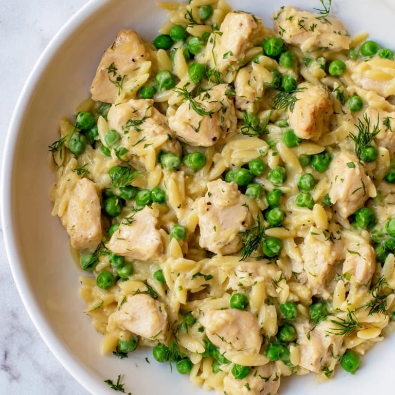 Golden chicken pieces and tender orzo pasta mixed with green peas in a zesty lemon herb sauce, served warm.