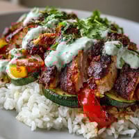 Golden-brown blackened chicken breast slices rest on fluffy white rice next to vibrant sautéed peppers and zucchini, drizzled with lime crema.